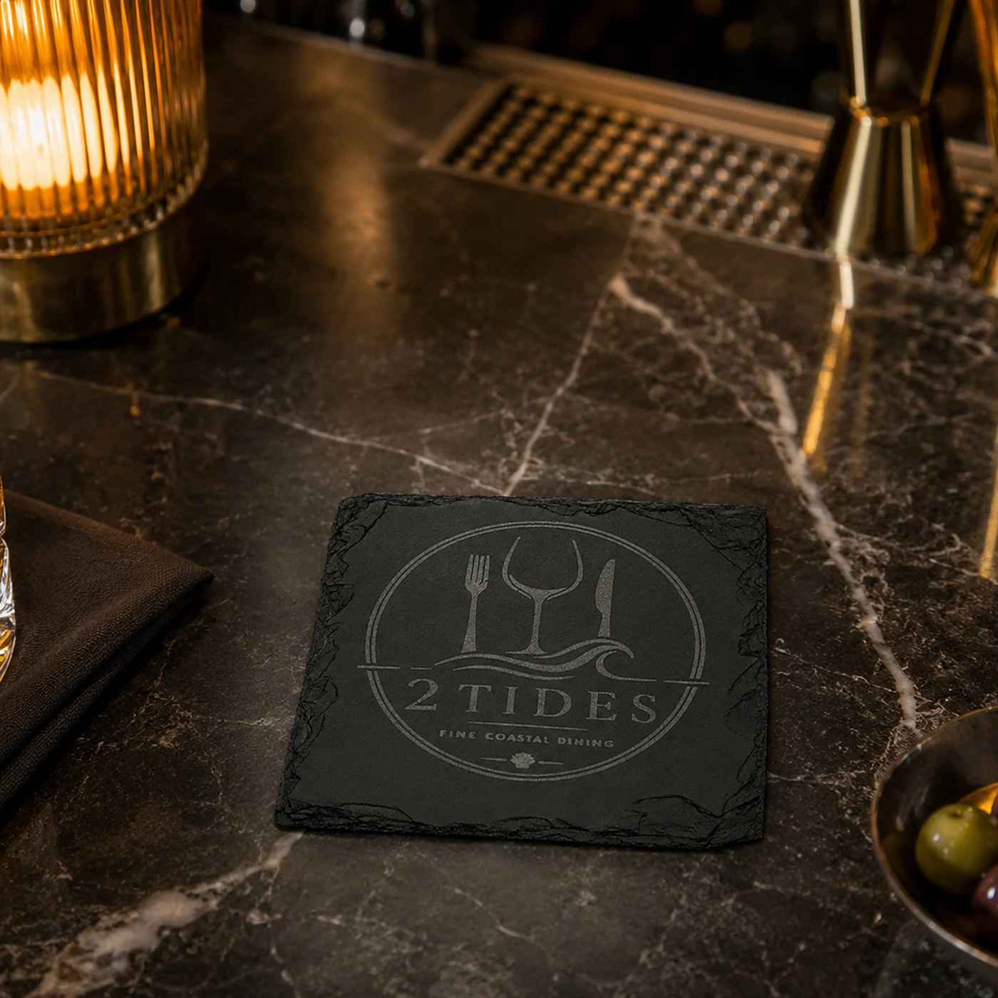 Schiefer Untersetzer mit lasergraviertem Firmenlogo auf einem Gastronomietisch neben einem Glas — Ansicht 1 von 8